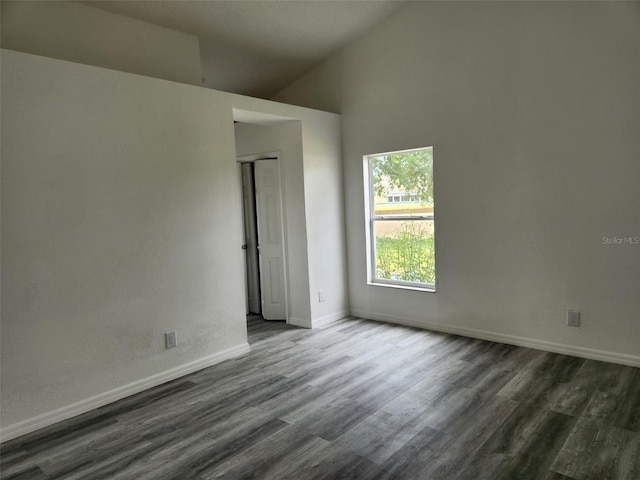 spare room with dark wood-type flooring, baseboards, and lofted ceiling