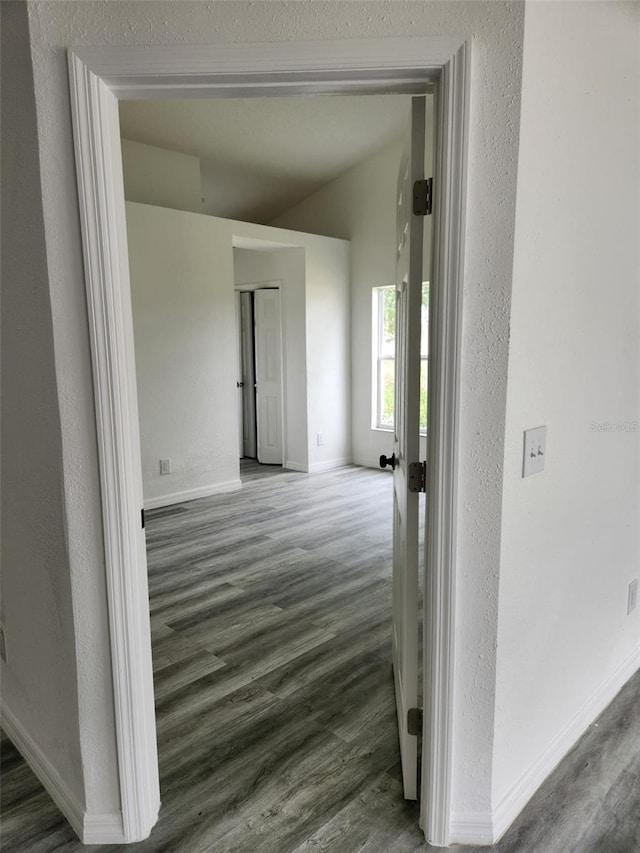 hallway featuring wood finished floors, baseboards, a textured wall, and vaulted ceiling