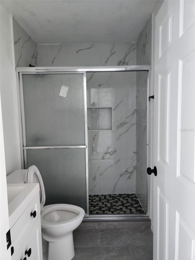 bathroom with a marble finish shower, toilet, marble look tile flooring, and vanity