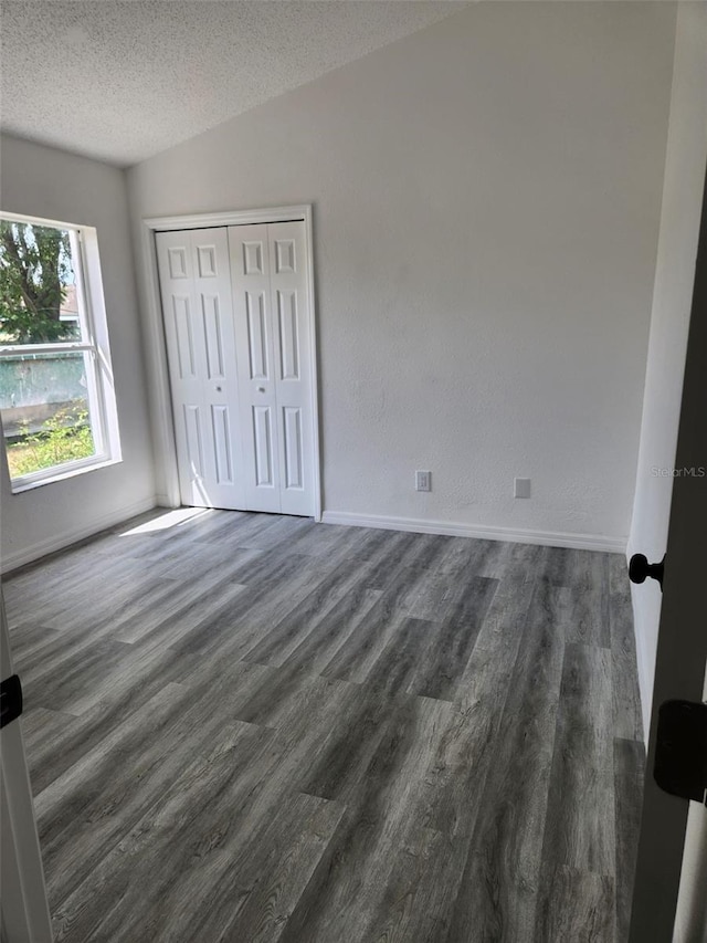 unfurnished bedroom featuring dark wood-style floors, a textured ceiling, a closet, and baseboards