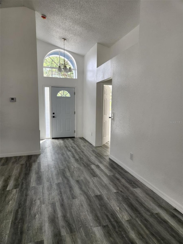 entrance foyer with a textured ceiling, dark wood-style floors, baseboards, a chandelier, and lofted ceiling