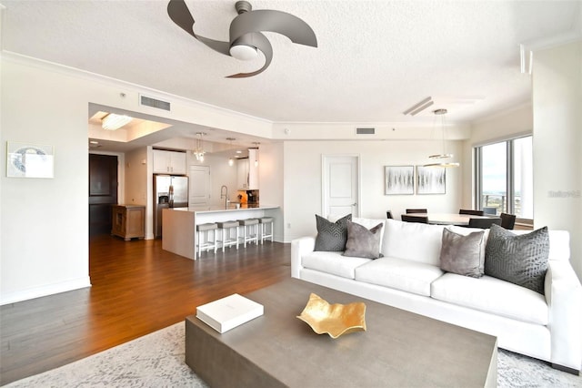 living room featuring a textured ceiling, dark wood finished floors, a ceiling fan, ornamental molding, and baseboards