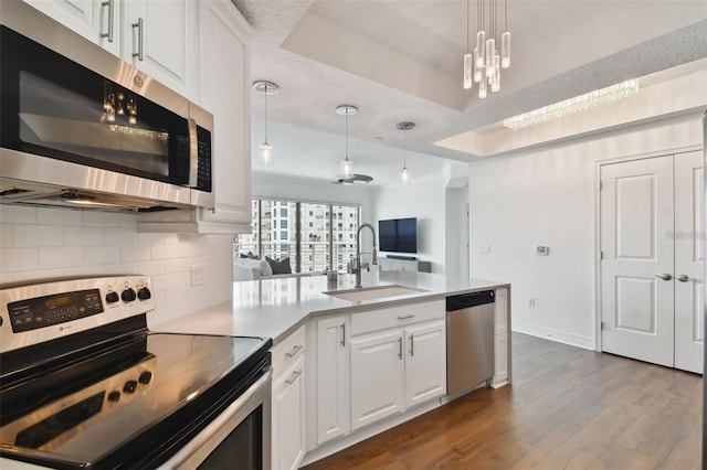 kitchen with stainless steel appliances, a sink, a peninsula, backsplash, and a raised ceiling