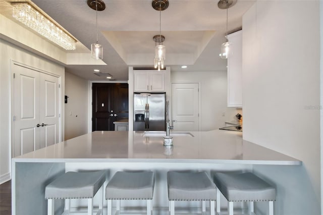 kitchen with stainless steel fridge with ice dispenser, a tray ceiling, white cabinetry, a breakfast bar area, and light countertops
