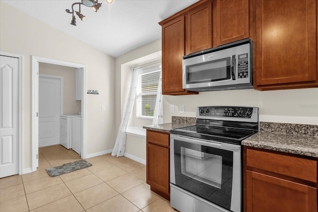 14617 Keelford Way, Orlando, FL 32824 - kitchen featuring stainless steel appliances, washing machine and dryer, lofted ceiling, light tile patterned floors, and dark stone counters