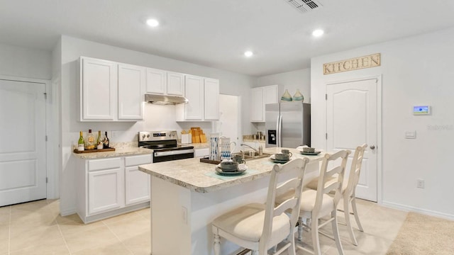 4912 Kaia Ave, Winter Haven, FL 33884 - kitchen with stainless steel appliances, under cabinet range hood, light countertops, white cabinets, and a kitchen breakfast bar