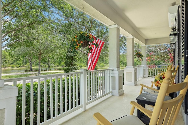 view of patio featuring a porch, a water view, and view of wooded area