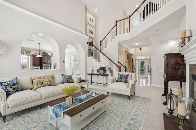 carpeted living room with a high ceiling, stairway, and arched walkways