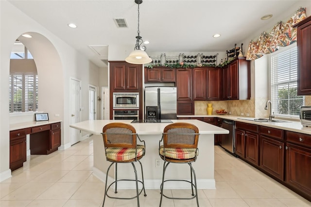 kitchen featuring appliances with stainless steel finishes, a sink, decorative backsplash, reddish brown cabinets, and healthy amount of natural light