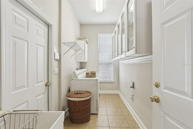 clothes washing area with cabinet space, light tile patterned floors, baseboards, and washer and clothes dryer
