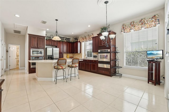 kitchen with appliances with stainless steel finishes, a warming drawer, light countertops, a center island, and baseboards