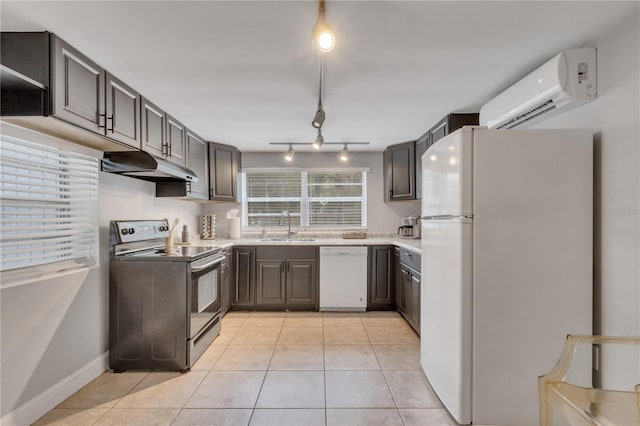 kitchen with white appliances, under cabinet range hood, a sink, a wall unit AC, and light tile patterned flooring