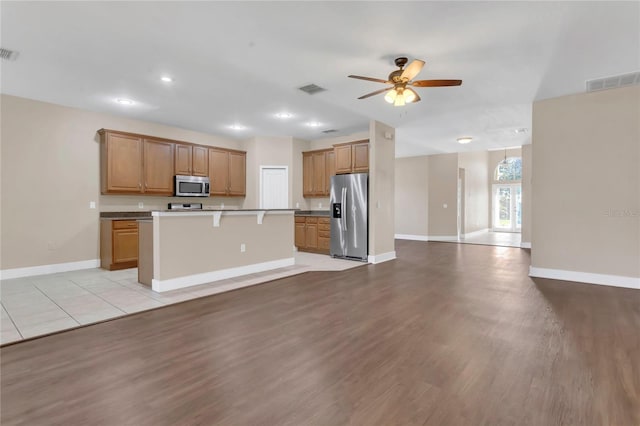 kitchen featuring appliances with stainless steel finishes, open floor plan, baseboards, ceiling fan, and light wood-style flooring