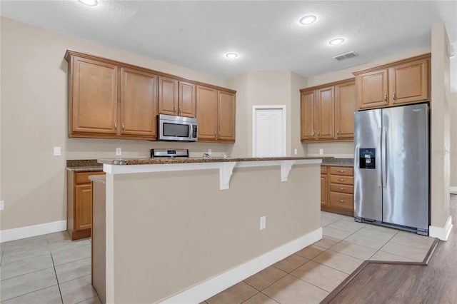 kitchen featuring stainless steel appliances, baseboards, a breakfast bar, a center island with sink, and a textured ceiling