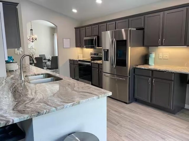 kitchen with appliances with stainless steel finishes, a sink, light stone countertops, arched walkways, and light wood finished floors