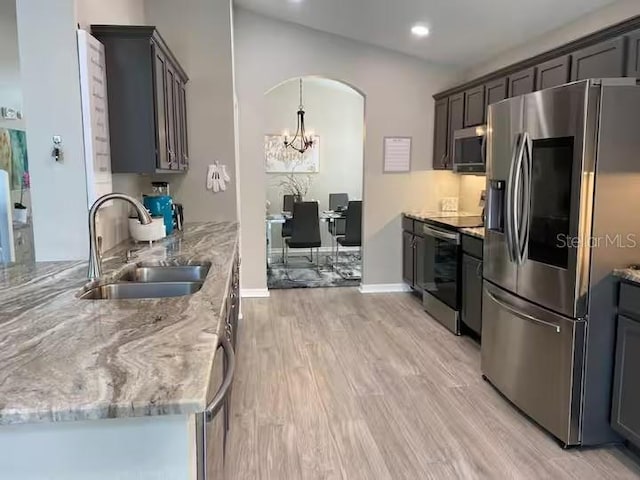 kitchen featuring appliances with stainless steel finishes, a sink, a chandelier, light stone counters, and light wood-style flooring