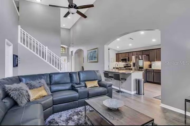living room featuring arched walkways, ceiling fan, light wood-style floors, recessed lighting, and stairway