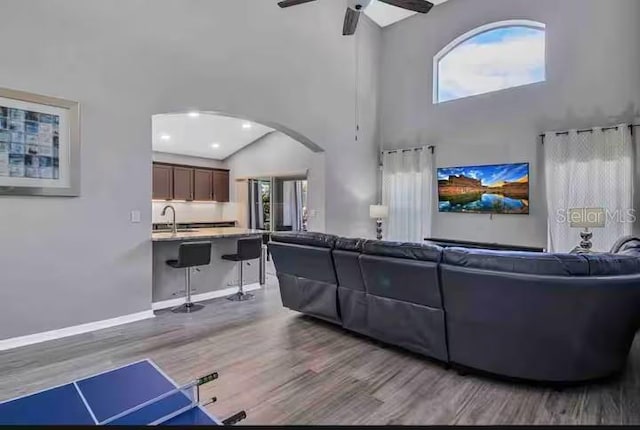 living room featuring a towering ceiling, wood finished floors, healthy amount of natural light, a ceiling fan, and arched walkways