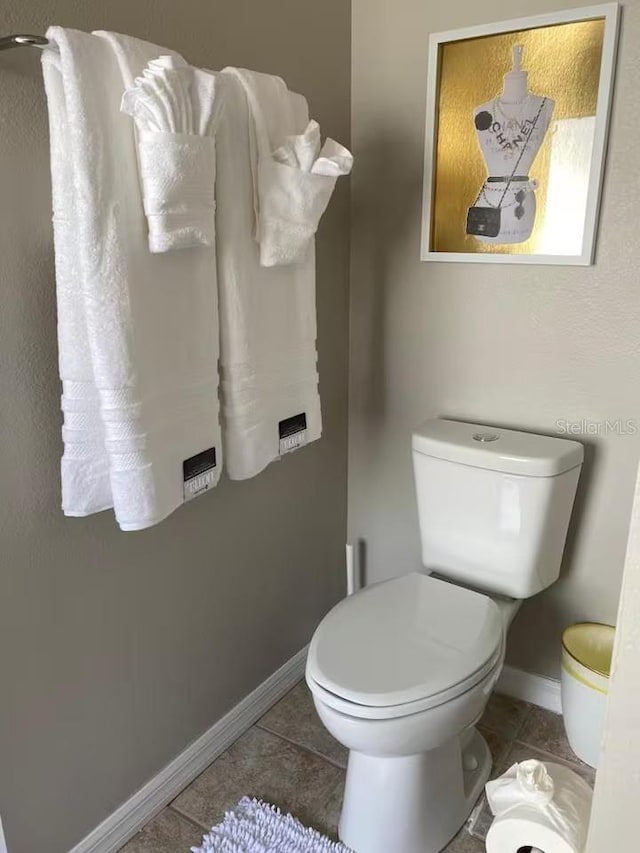 half bathroom featuring tile patterned floors, baseboards, and toilet