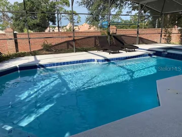 view of swimming pool featuring glass enclosure, fence, a patio area, and a pool with connected hot tub
