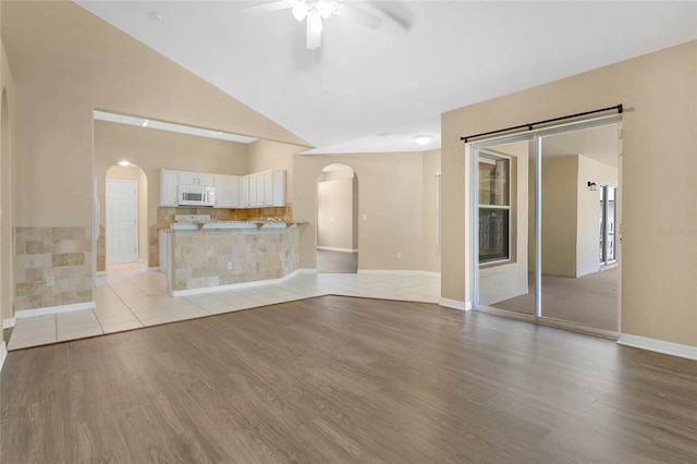 922 Hatteras Ave, Minneola, FL 34715 - unfurnished living room with arched walkways, ceiling fan, light wood-style floors, baseboards, and high vaulted ceiling