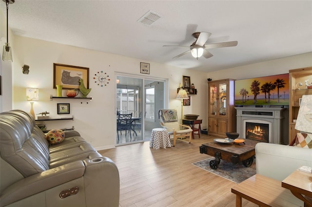 living room featuring light wood finished floors, ceiling fan, a lit fireplace, and baseboards