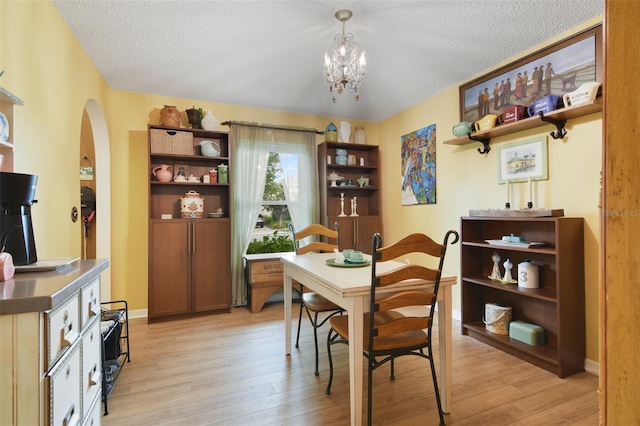 dining area featuring arched walkways, a textured ceiling, light wood-type flooring, a chandelier, and baseboards