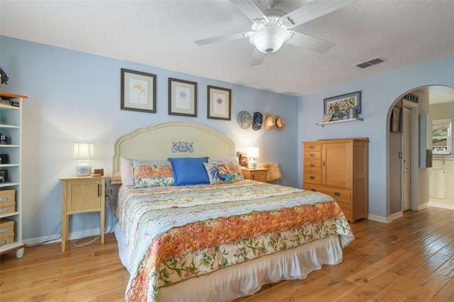 bedroom featuring arched walkways, light wood finished floors, baseboards, a textured ceiling, and ceiling fan