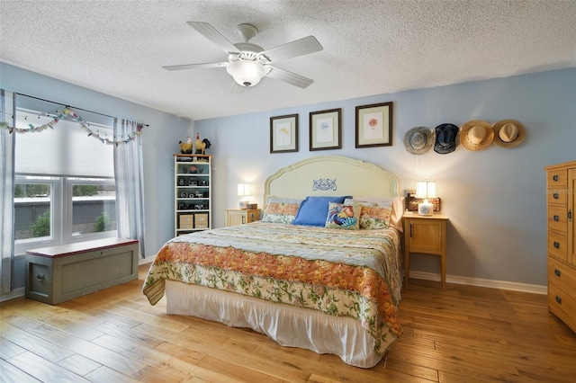 bedroom with light wood-type flooring, a textured ceiling, baseboards, and a ceiling fan