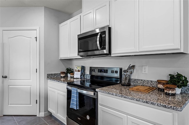kitchen featuring appliances with stainless steel finishes, dark stone counters, white cabinetry, and dark tile patterned flooring