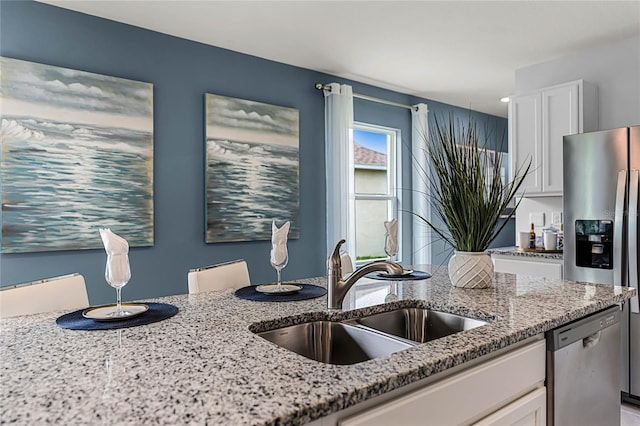 kitchen featuring appliances with stainless steel finishes, a sink, light stone countertops, and white cabinetry