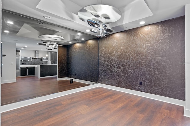 unfurnished room featuring a chandelier, a raised ceiling, wood finished floors, recessed lighting, and baseboards