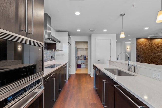 kitchen featuring a sink, wall chimney exhaust hood, appliances with stainless steel finishes, dark brown cabinetry, and pendant lighting