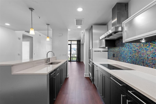 kitchen featuring a sink, wall chimney exhaust hood, black electric cooktop, light countertops, and decorative backsplash