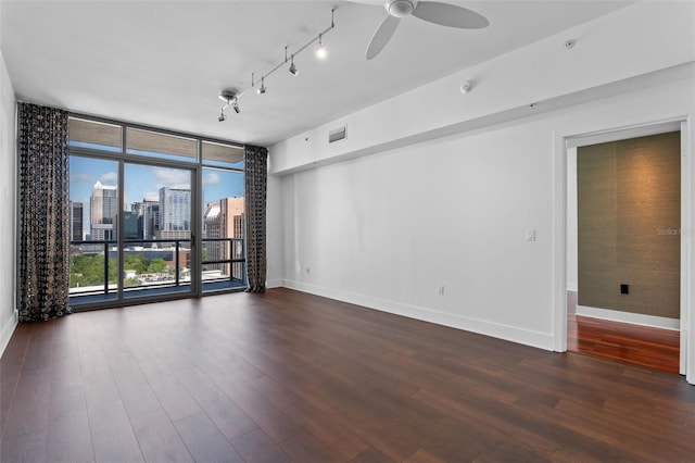 empty room with expansive windows, baseboards, dark wood-style flooring, a ceiling fan, and a view of skyline