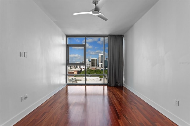 spare room featuring floor to ceiling windows, wood-type flooring, baseboards, a view of city, and ceiling fan