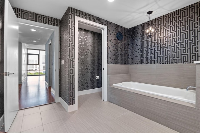bathroom with wallpapered walls, tiled bath, tile patterned floors, baseboards, and a chandelier