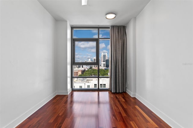 spare room featuring expansive windows, dark wood-type flooring, baseboards, and a view of city