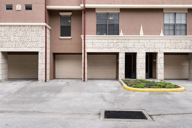 multi unit property with stucco siding, an attached garage, and stone siding
