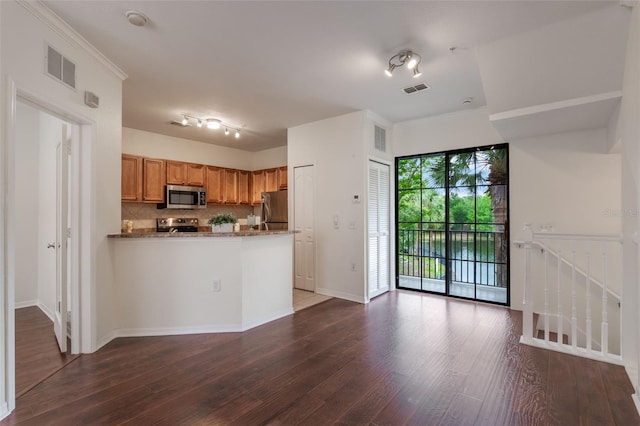 kitchen with appliances with stainless steel finishes, dark wood-style floors, a peninsula, decorative backsplash, and brown cabinetry
