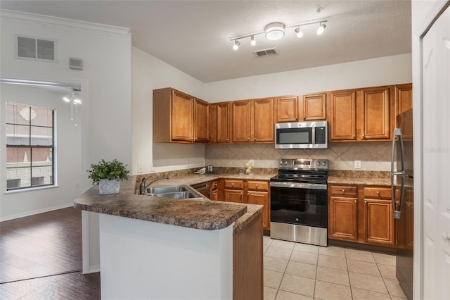 kitchen with appliances with stainless steel finishes, a sink, a peninsula, and brown cabinetry