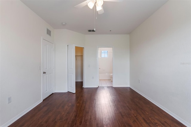 unfurnished bedroom with a spacious closet, wood finished floors, a closet, baseboards, and ensuite bath