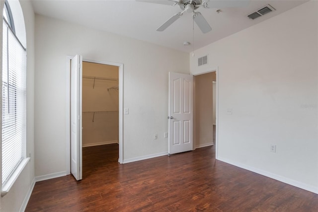 unfurnished bedroom with dark wood-style floors, a spacious closet, a closet, and baseboards