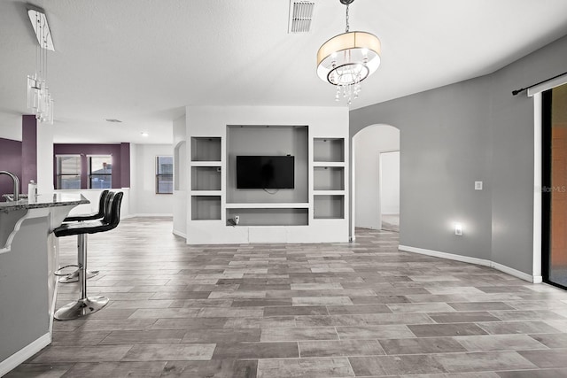 living room featuring arched walkways, baseboards, wood finished floors, built in shelves, and a chandelier