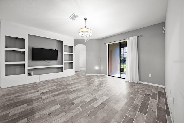 unfurnished living room featuring arched walkways, baseboards, built in features, and wood finished floors