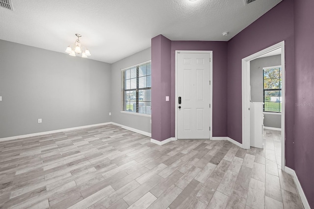 foyer entrance with a textured ceiling, a chandelier, light wood finished floors, healthy amount of natural light, and baseboards