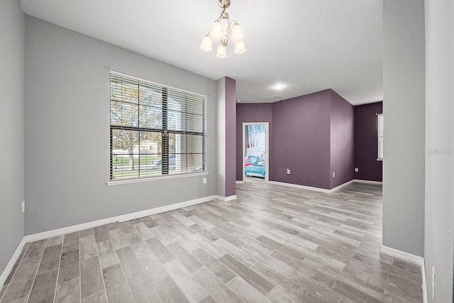 empty room featuring a chandelier, light wood-style flooring, and baseboards