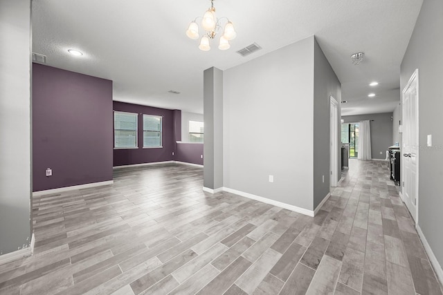 empty room featuring healthy amount of natural light, light wood-type flooring, a chandelier, and recessed lighting