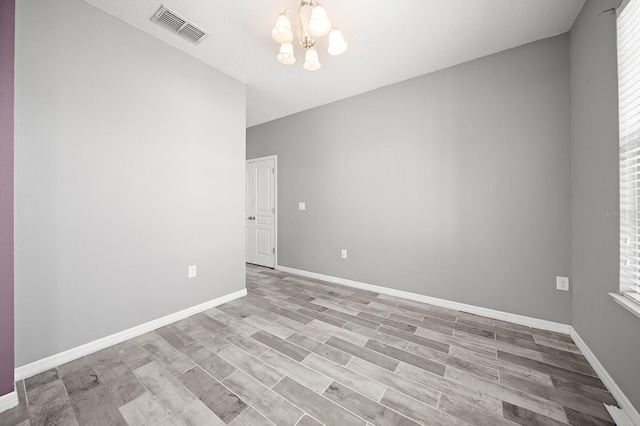 spare room featuring a chandelier, baseboards, and wood finished floors