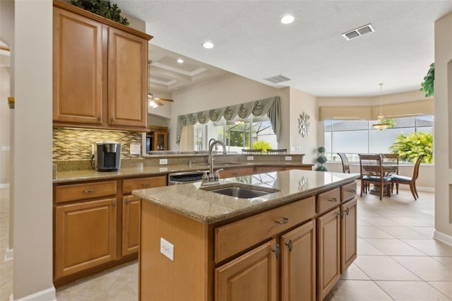 724 Duff Dr, Winter Garden, FL 34787 - kitchen with light stone counters, decorative backsplash, light tile patterned floors, a kitchen island with sink, and brown cabinetry